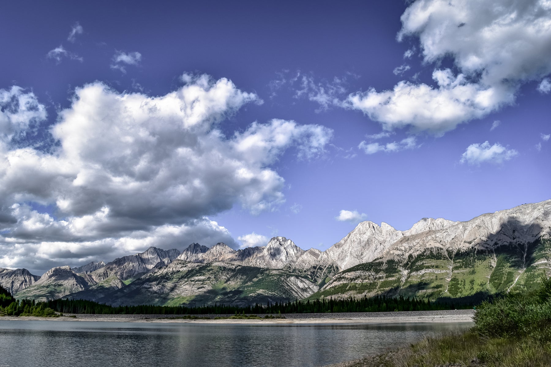 beautiful outdoor photo of mountains and a lake with a blue sky and clouds.