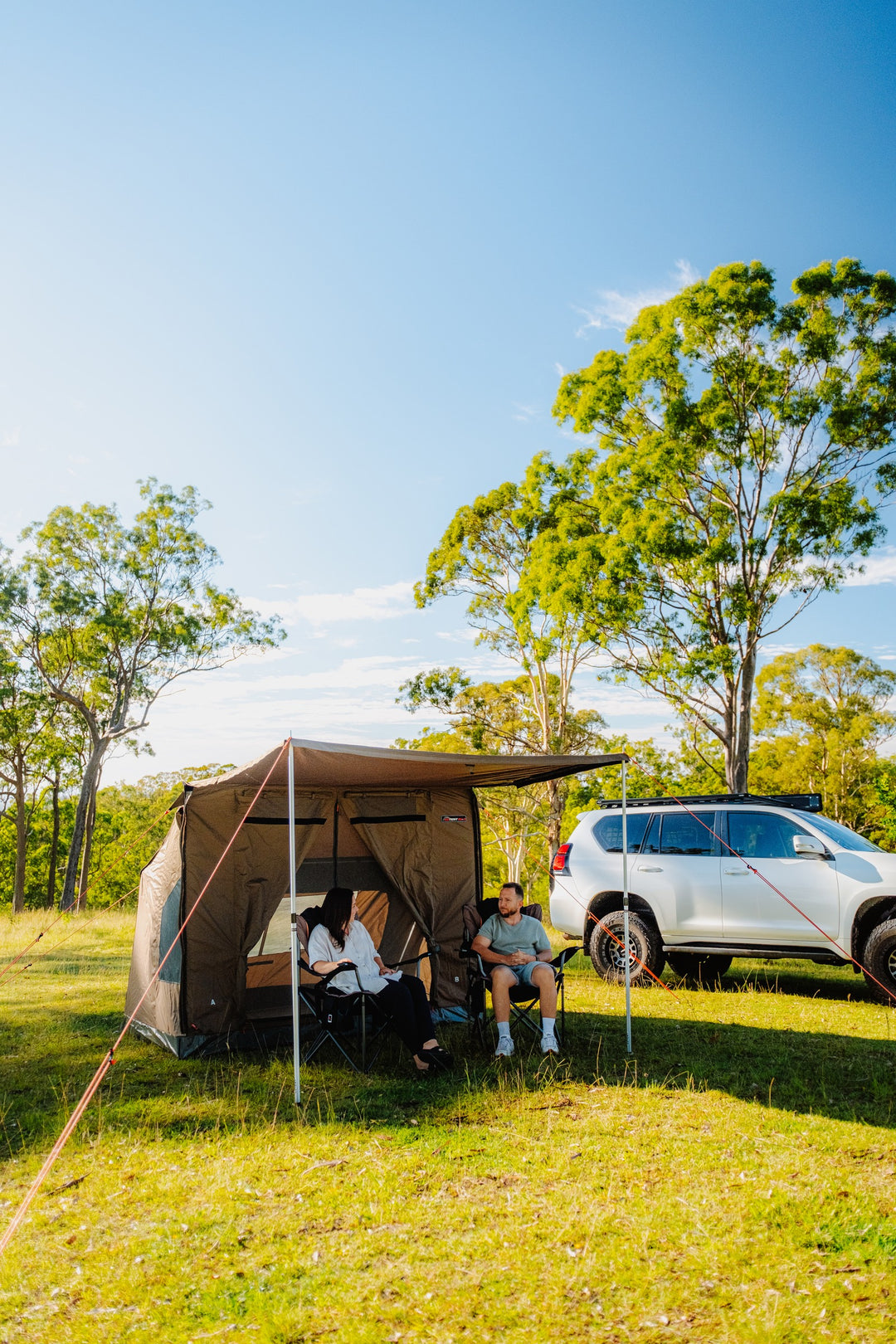 Oztent RV-3 tent beside a vehicle with campers beneath the awning