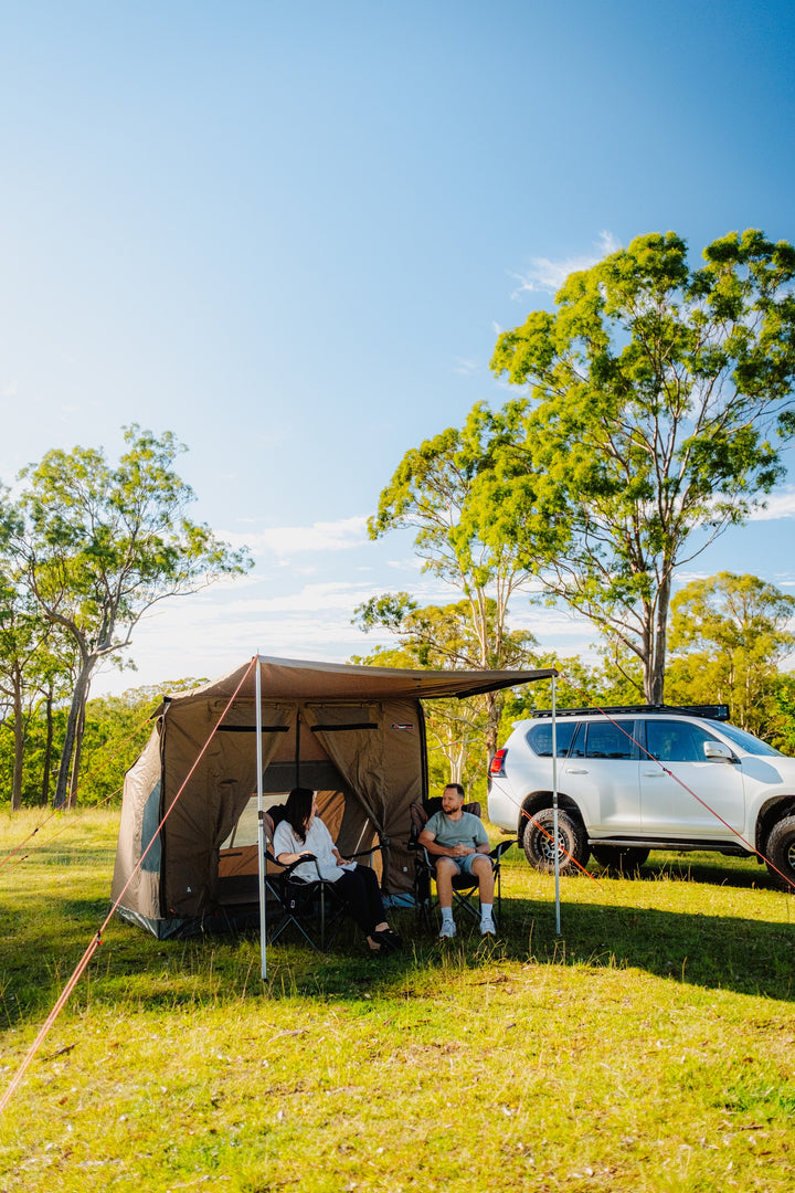 Oztent RV-3 tent beside a vehicle with campers beneath the awning