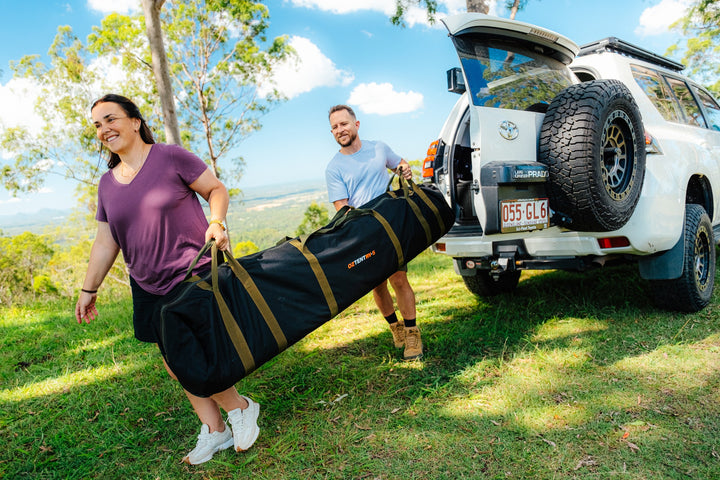 Campers carrying an Oztent RV-5 tent bag from their vehicle