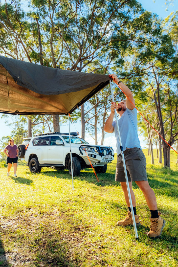 Camper raising the Oztent RV-5 awning at a wooded campsite